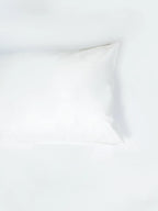 Plain white pillowcase resting on white bedding