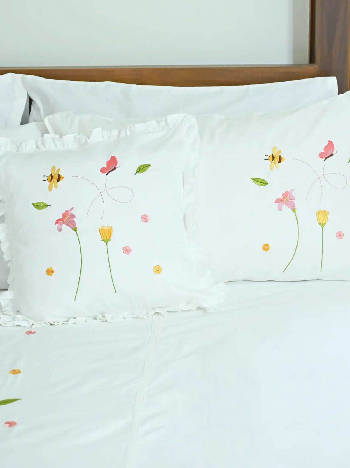Bees and Blossom white embroidered pillowcases arranged on a bed