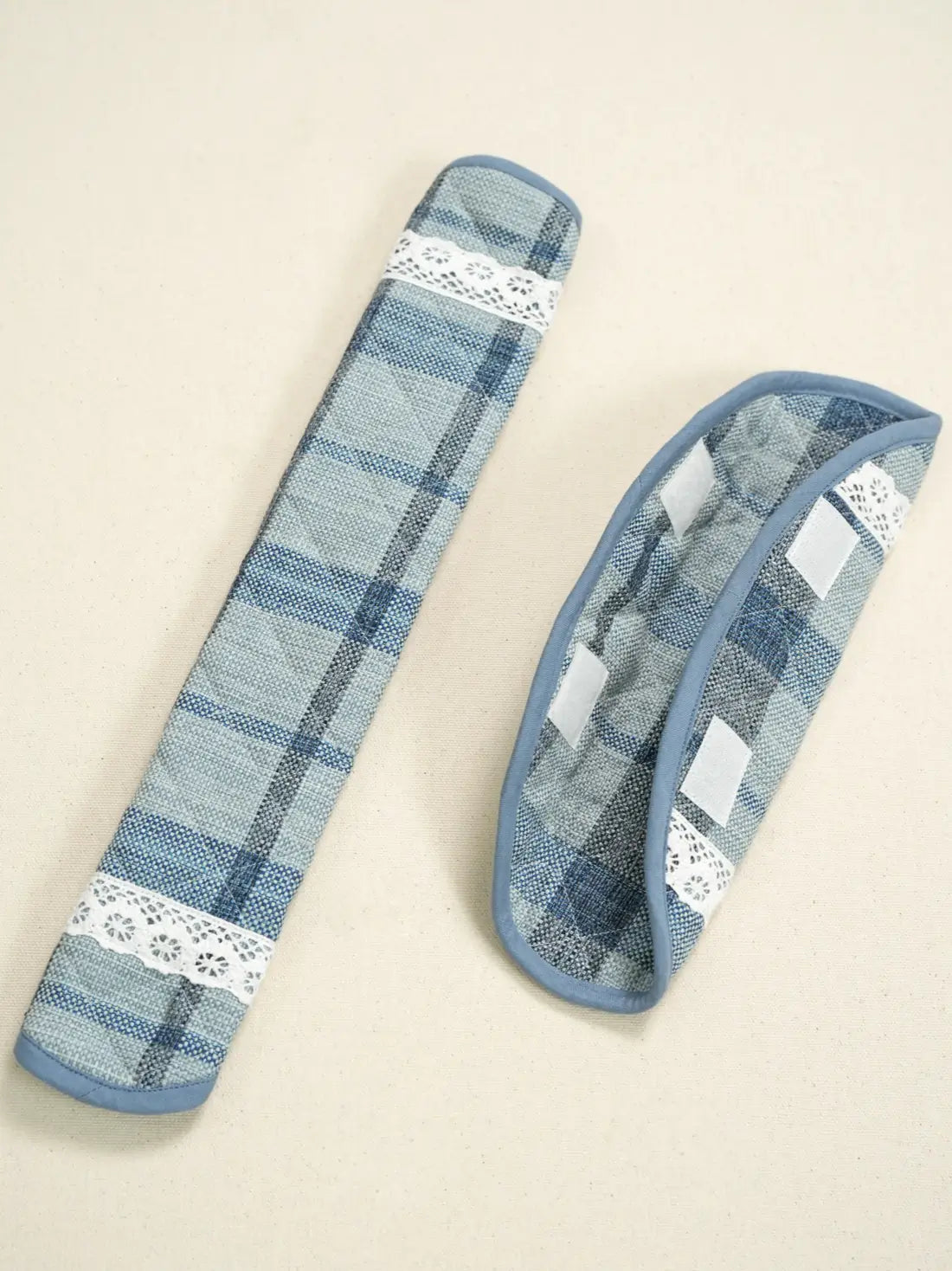Two blue plaid fabric handle covers with white lace trim and hook-and-loop tabs