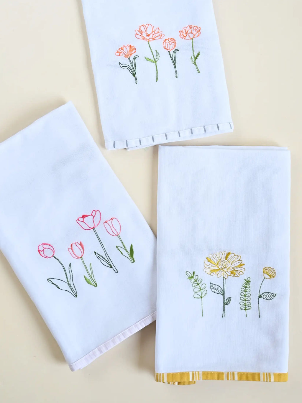 Three white Kerala bath towels with pink, orange and yellow floral embroidery and coloured border trims