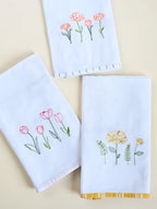 Three white Kerala bath towels with pink, orange and yellow floral embroidery and coloured border trims