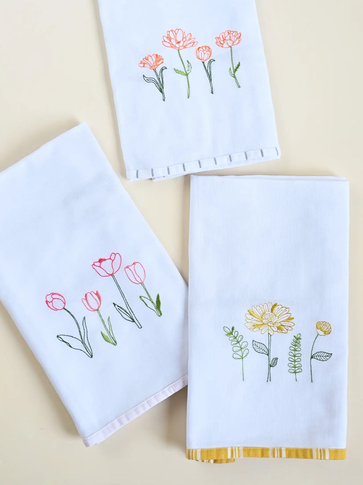 Three white Kerala bath towels with pink, orange and yellow floral embroidery and coloured border trims