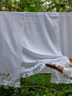 Three white embroidered Kerala bath towels hanging outdoors, with a hand holding the centre towel