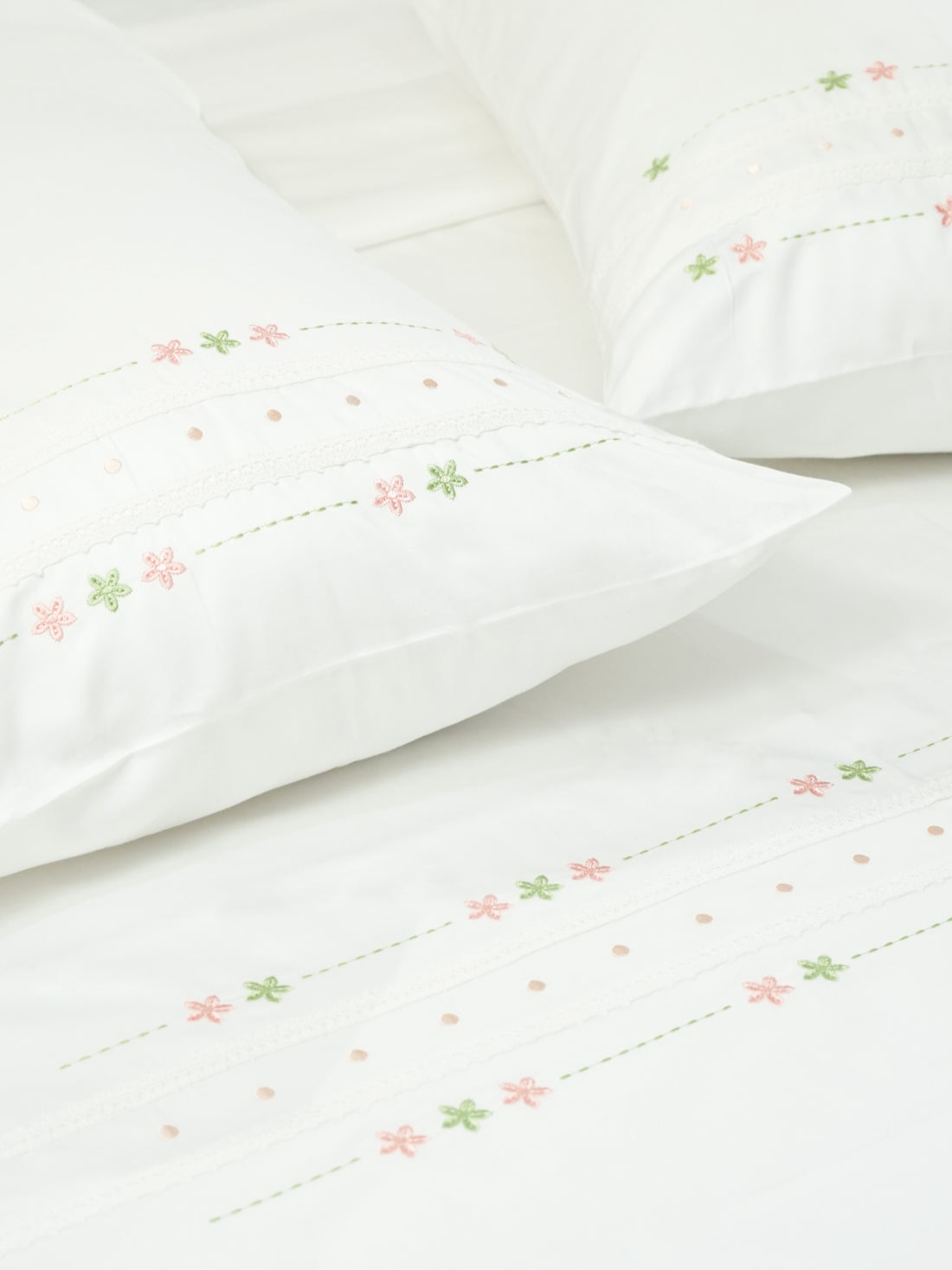 White bed sheet and pillowcases with pink and green floral embroidery, lace bands and dotted details