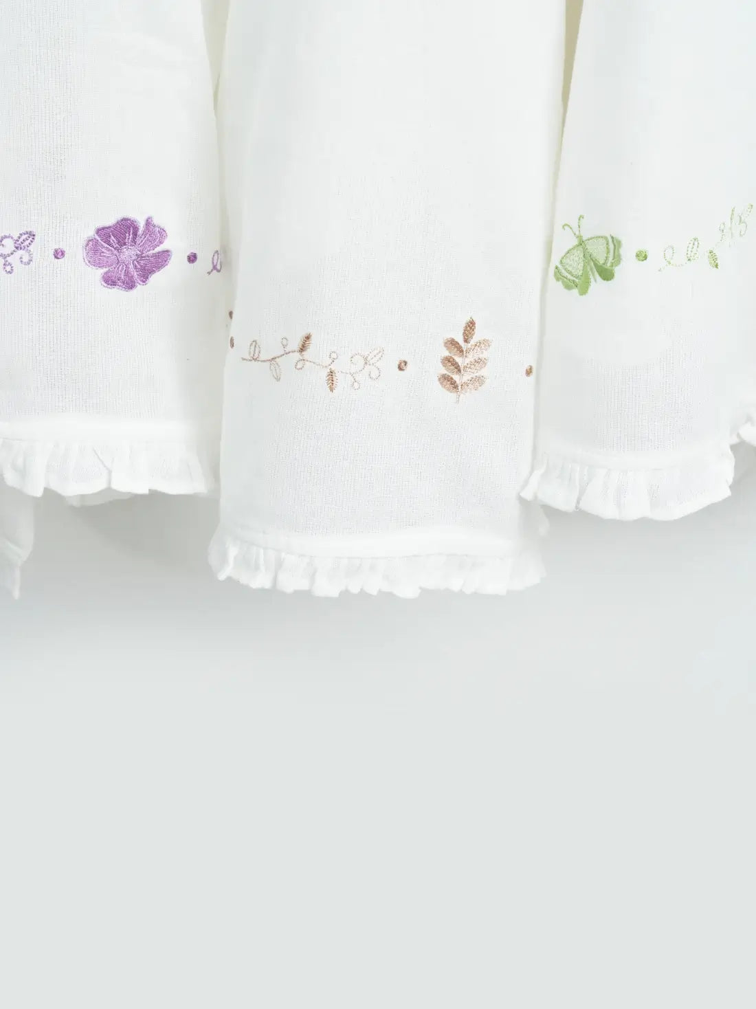 Close-up of three white Thorthu towels with floral embroidery and ruffled hems