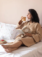 Woman wearing a French beige waffle bath robe while reading on a bed