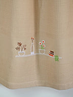 Close-up of potted plants, flowers, a bottle and books embroidered on a cream honeycomb towel