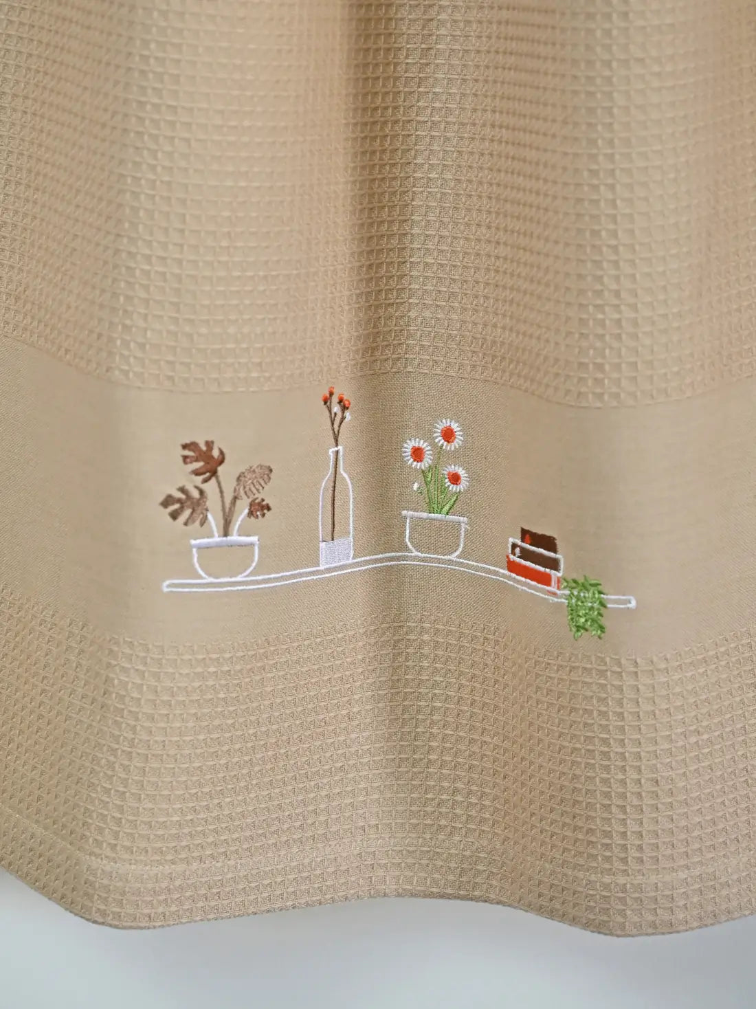Close-up of potted plants, flowers, a bottle and books embroidered on a cream honeycomb towel