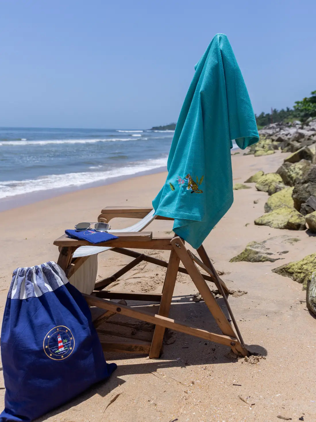 Navy blue lighthouse-embroidered laundry bag beside a beach chair with a teal towel