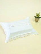 White lace-trimmed tissue box cover with two ribbon bows beside a small potted plant