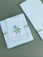 Three folded pale blue waffle towels with blue flowers and green vine embroidery
