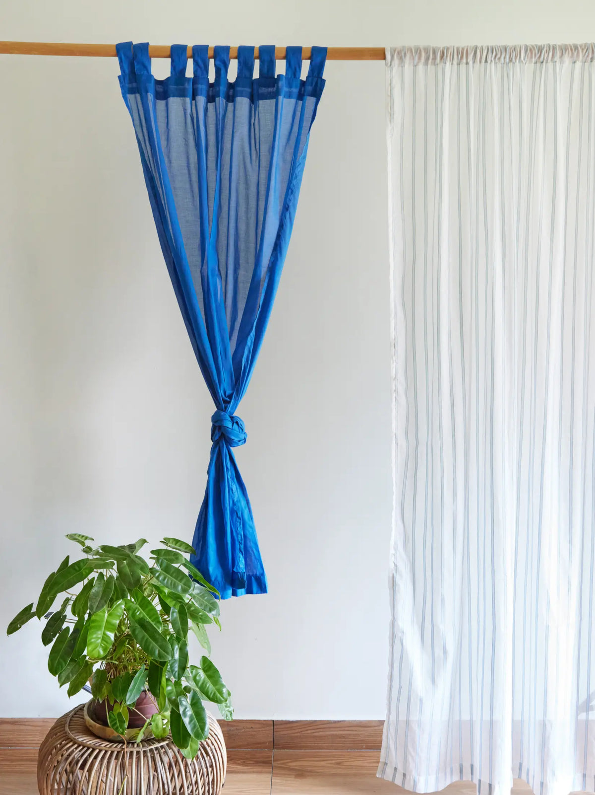 Blue sheer curtain tied at the centre beside a white striped curtain