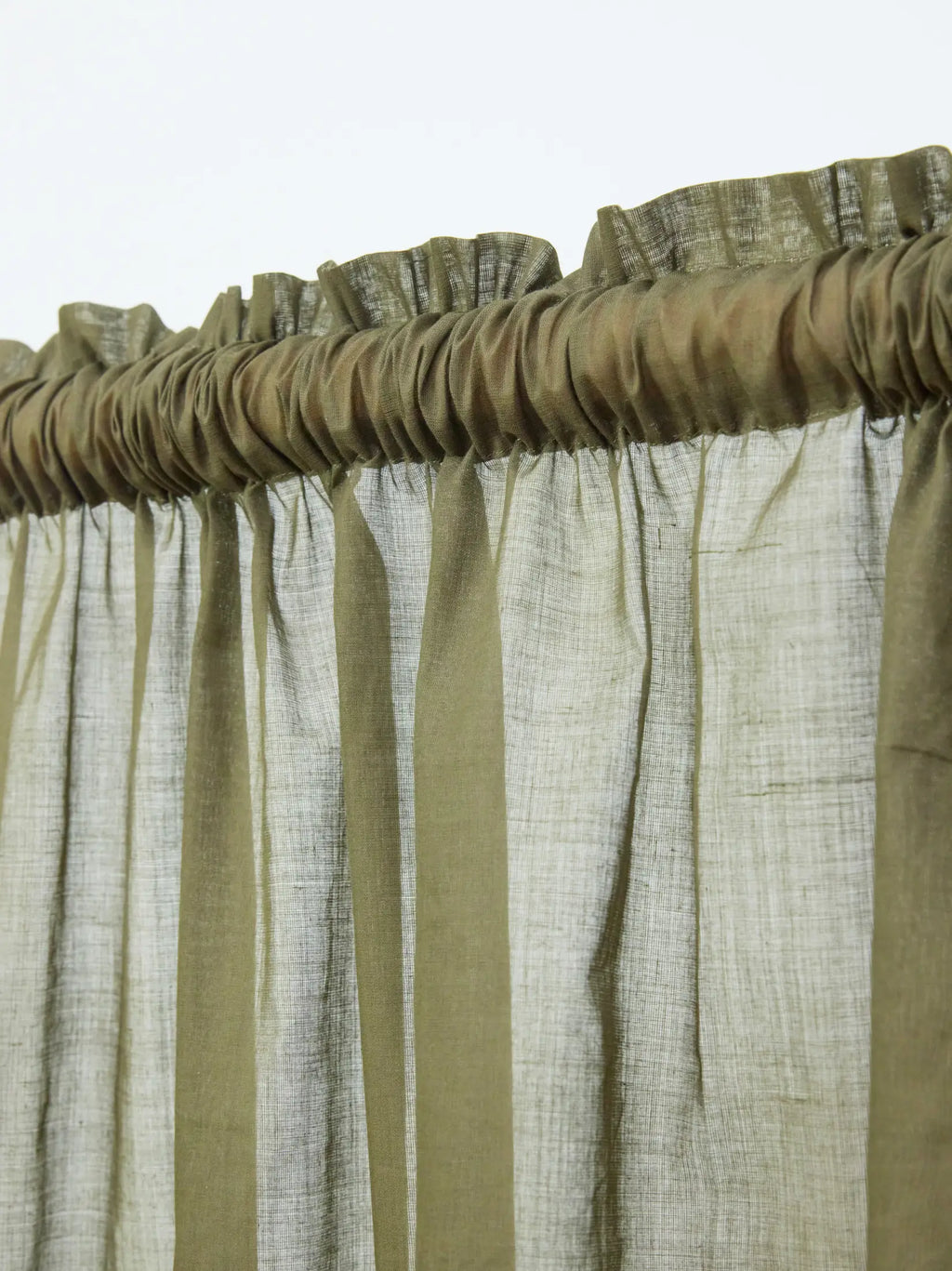 Close-up of olive green sheer curtain gathered on a wooden rod