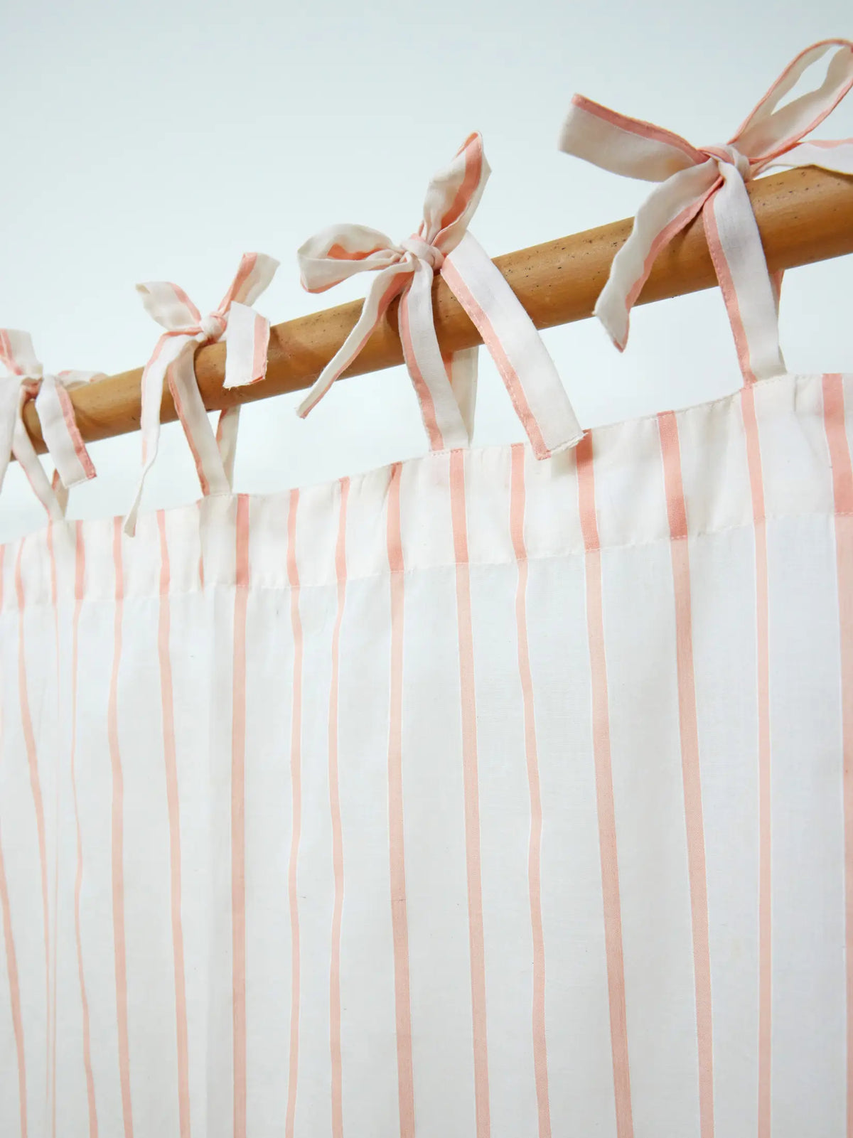 Close-up of fabric tie-top bows on a peach striped sheer curtain