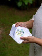 White handkerchief with blue floral embroidery and lace edge held outdoors
