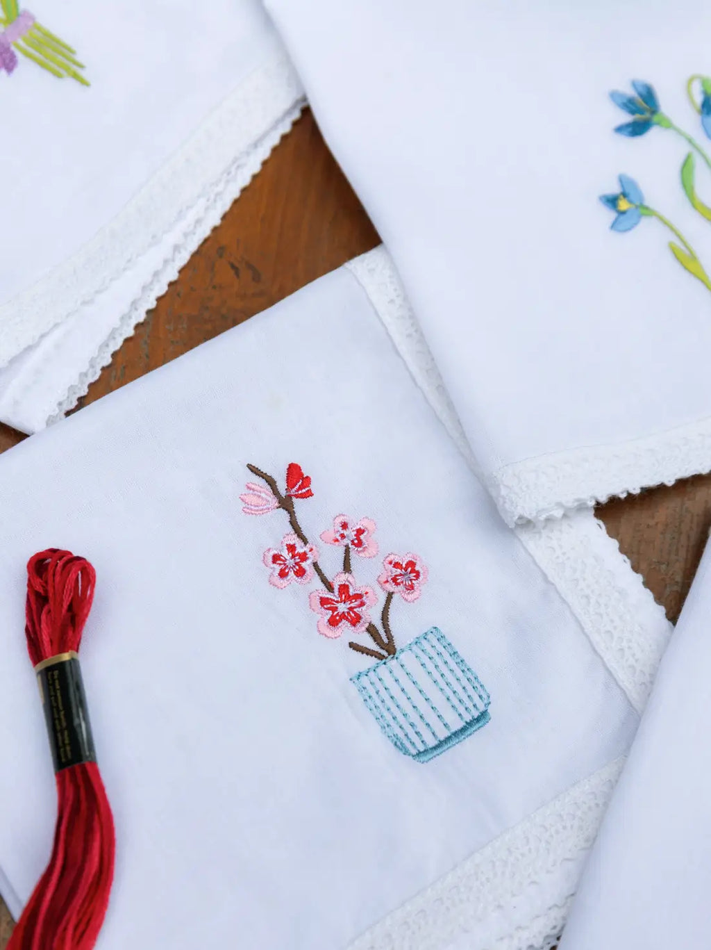 White lace-edged handkerchief embroidered with pink blossoms in a pale blue striped pot