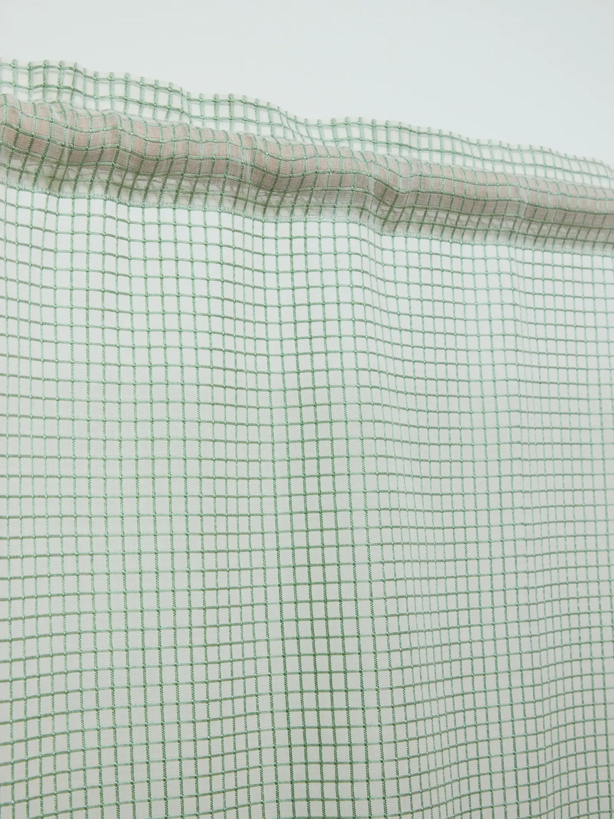 Close-up of the gathered rod pocket and green grid pattern on a white sheer curtain