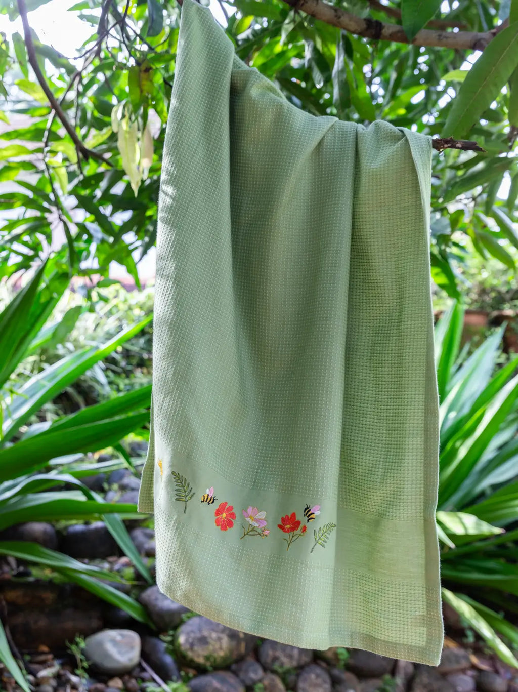 Olive green waffle towel with bee and garden flower embroidery hanging from a tree branch