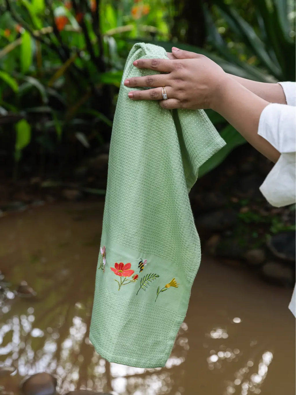 Hands holding an olive green waffle towel with bee and garden flower embroidery