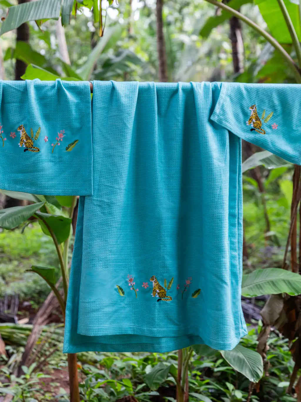 Three teal blue waffle towels with tiger and flower embroidery hanging outdoors
