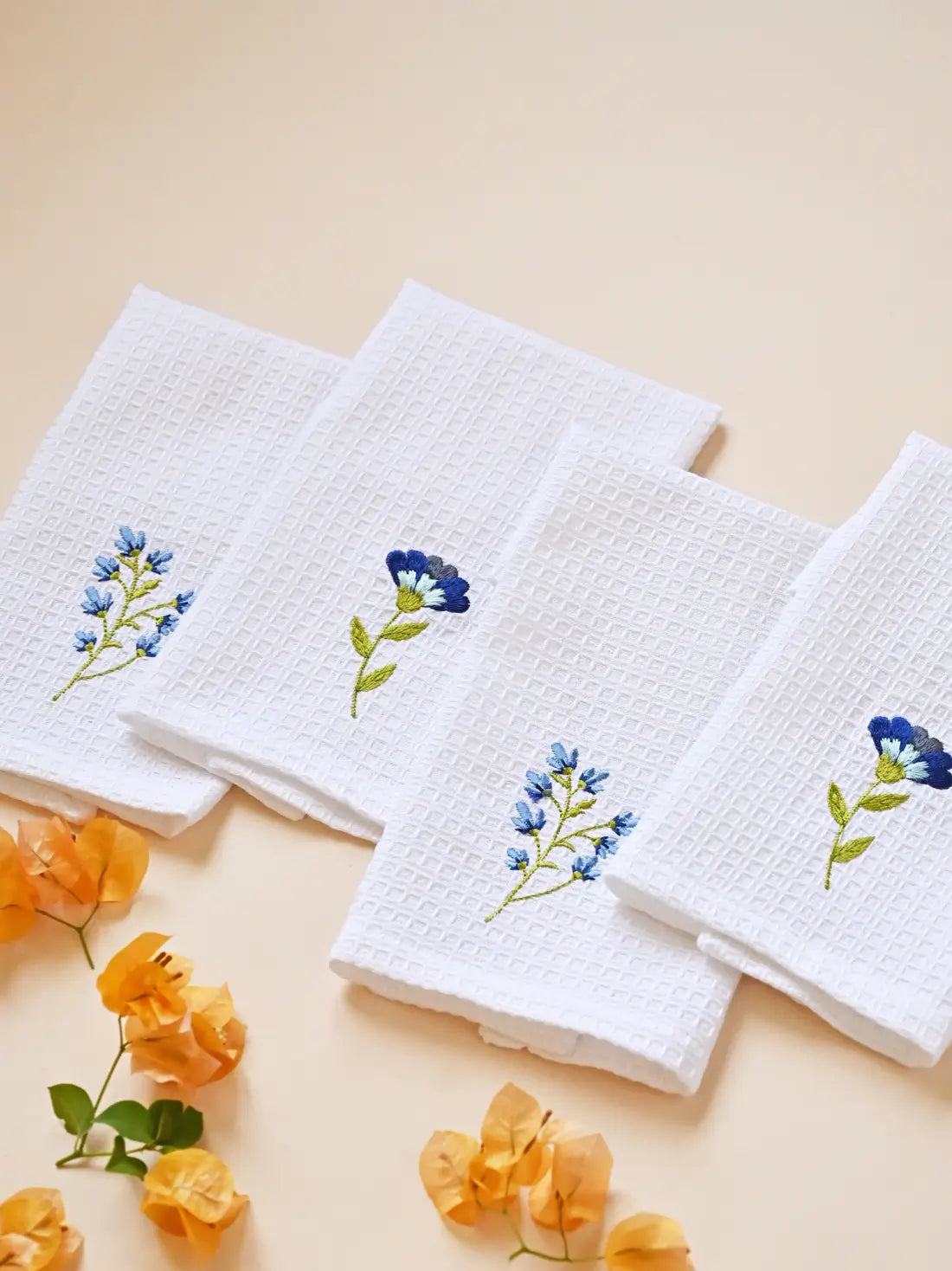 Four white waffle face towels arranged to show two blue embroidered flower designs