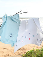 Pale blue and white waffle towels with embroidered anchors and ship wheels hanging by the beach