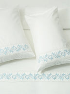 White bed linen and two pillowcases with blue vine embroidery and white lace trim