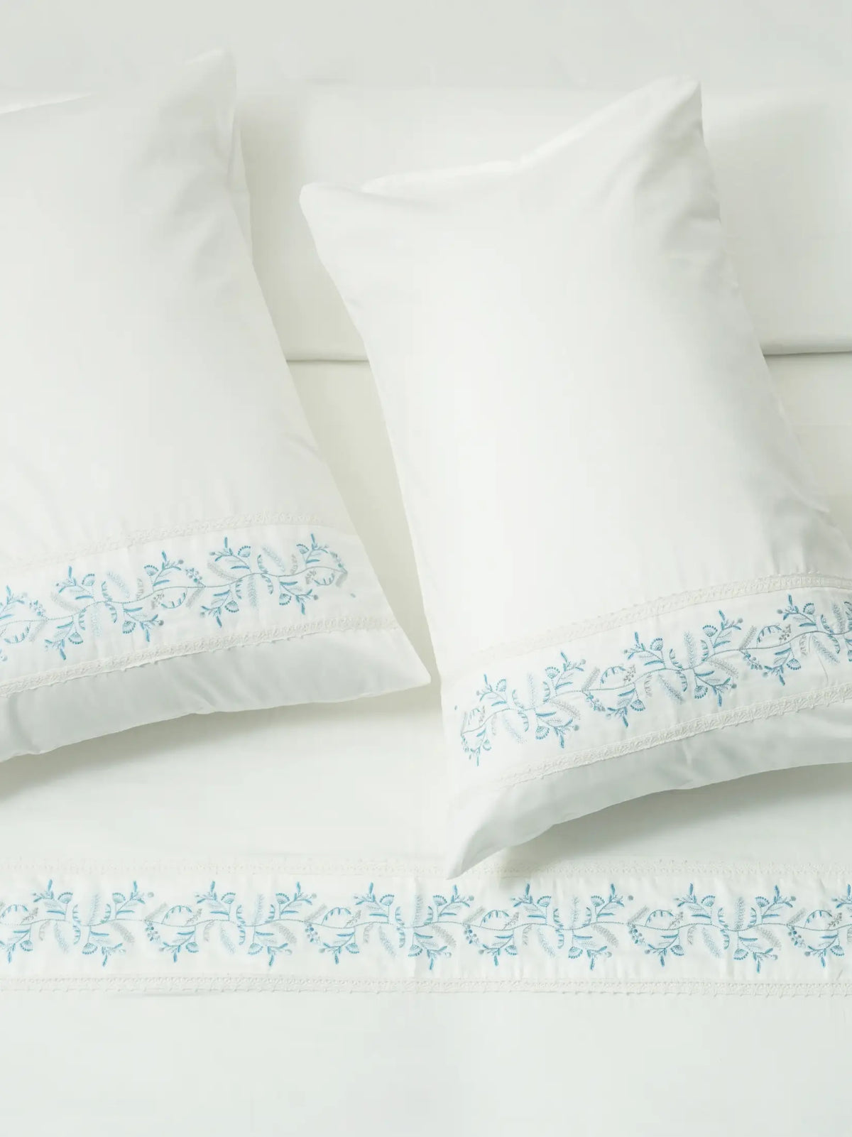 White bed linen and two pillowcases with blue vine embroidery and white lace trim