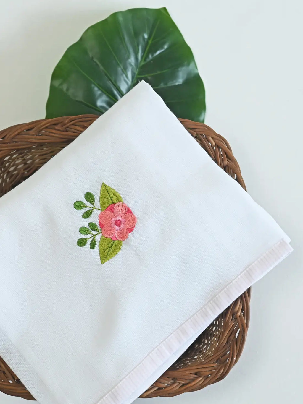 White Kerala Thorthu towel with pink flower embroidery in a wicker basket