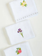 Three folded white Kerala Thorthu towels with yellow, purple and pink floral embroidery